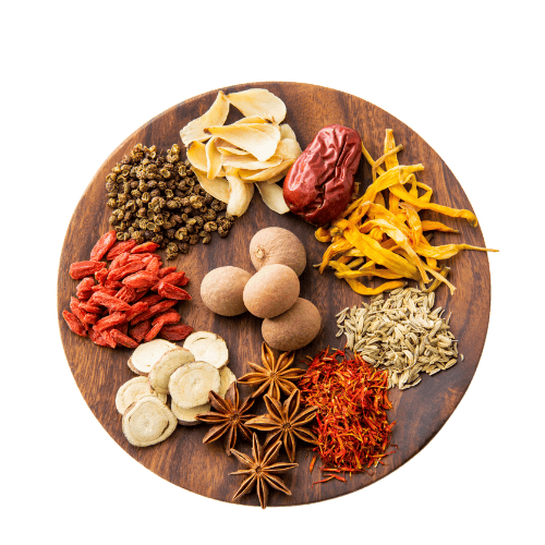 Food as medicine A round wooden plate neatly arranged with a colorful assortment of dried herbs and spices, including star anise, goji berries, dried mushrooms, fennel seeds, dried jujube, safflower petals, sliced ginseng, and yellow flower petals. Each ingredient is placed in its own section, creating a visually balanced and aromatic display.
