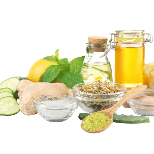 natural skincare A collection of natural skincare or wellness ingredients arranged on a white background, featuring sliced cucumber, fresh ginger, a lemon with mint leaves, dried herbs, aloe vera, and a variety of oils and powders in glass containers and bowls. A wooden spoon holds coarse green crystals, suggesting a homemade spa or beauty remedy setup.