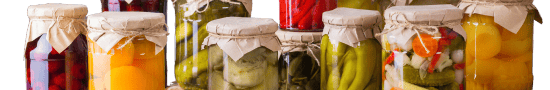 assorted jars A row of assorted glass jars filled with brightly colored preserved foods, including pickles, beets, peppers, cucumbers, and mixed vegetables. Each jar is sealed with rustic brown paper and twine, creating a homemade, pantry-style presentation.